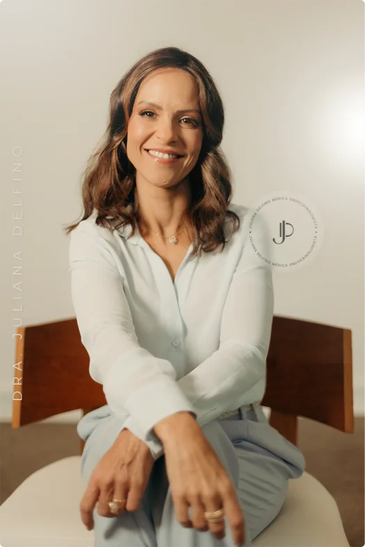 Imagem da Dra. Juliana Delfino, Endocrinologista em Brasília, mulher branca, sorrindo e sentada usando roupa clara.