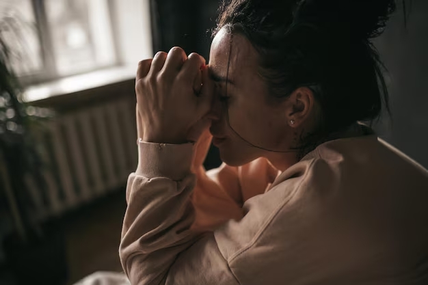 Mulher com sinais de ansiedade e estresse, sentada com as mãos no rosto em momento de preocupação