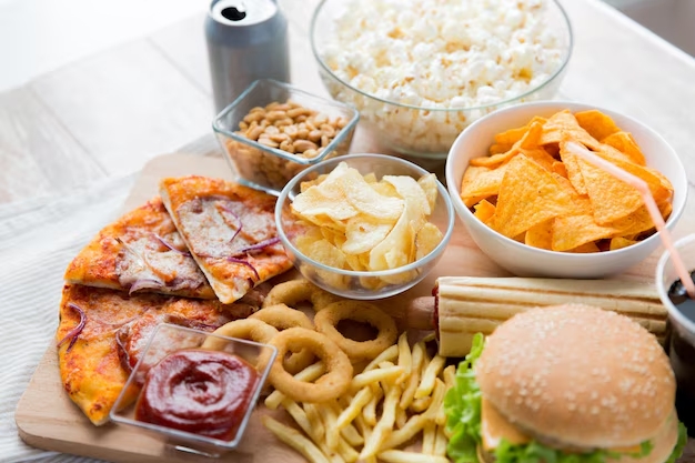 Mesa com pizza, hambúrguer, batata frita, salgadinhos e refrigerante, exemplo de ultraprocessados